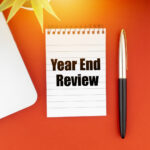 34809282_year-end-review-text-with-notepad-laptop-fountain-pen-and-decorative-plant-on-red-background